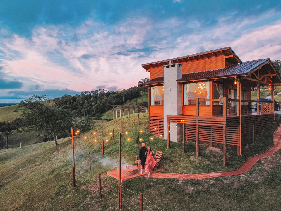 Chalé Mirante ao entardecer, com casal no deck e luzes no gramado